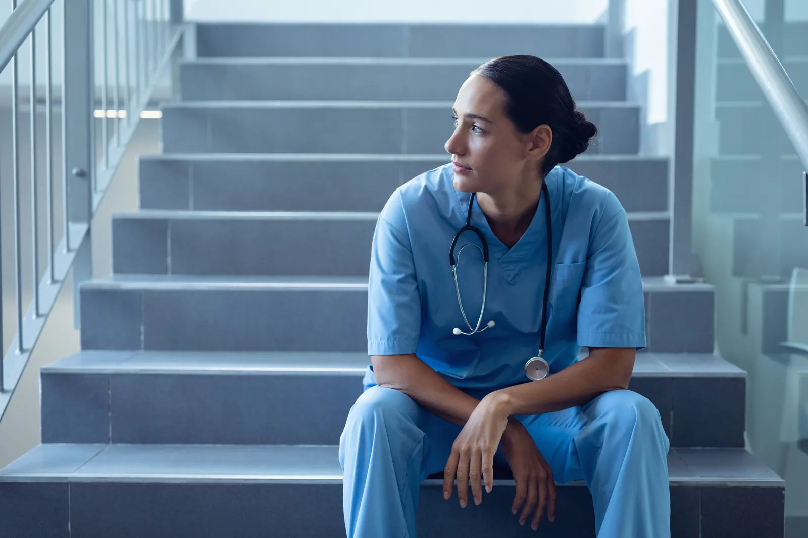 Krankenpflegerin sitzt nachdenklich auf einer Treppe im Krankenhaus